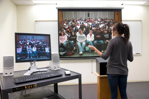 woman standing at podium in front of screen with students looking back 