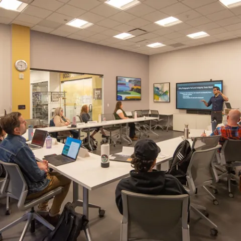 Faculty in front of a whiteboard lecturing to a small group of students